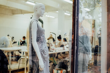 Mannequins in display window inside of fashion clothes manufacture. Design, studio for sewing and cutting clothes, designer clothes, manufacturing, craft product. Educational center. Selective focus.