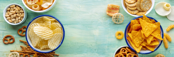 Salty snacks panorama, overhead flat lay background with copy space. Party food frame. Potato and tortilla chips, salt crackers and other appetizers