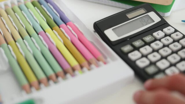 Child Hands With Calculator Counting During School Homework And Colorful Crayons On Table. Kid Fingers Press Buttons And Calculate Doing Math Closeup