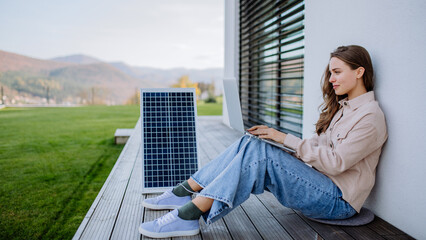 Young woman sitting on terrace, charging tablet trough solar panel.