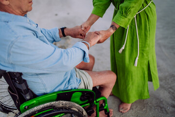 Close-up of senior woman holding hands her husband on wheelchair, enjoying vacations together.