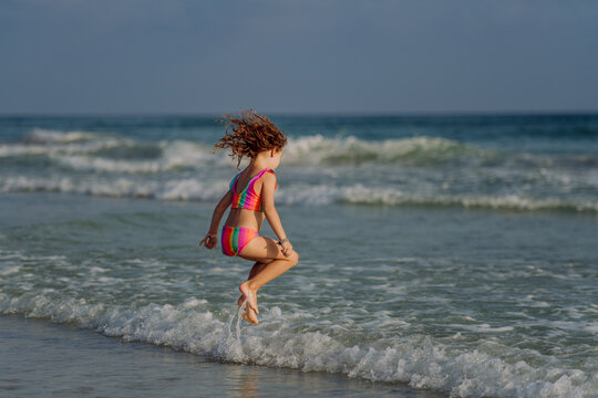 Little girl in swimsuit jumping in sea, enjoying holiday.
