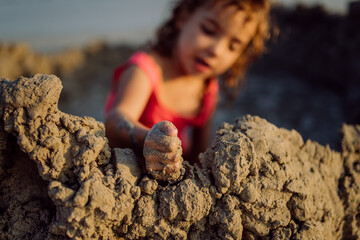 Little girl playing on the beach, digging hole in sand.