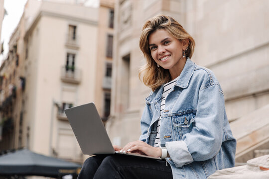 Picture of beautiful european woman have chatting on laptop. Wearing jacket looking and smiling at camera, working outdoors. Concept of student life 