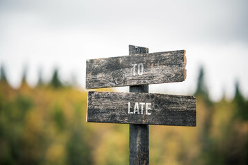 vintage and rustic wooden signpost with the weathered text quote to late, outdoors in nature. blurred out forest fall colors in the background.