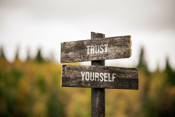 vintage and rustic wooden signpost with the weathered text quote trust yourself, outdoors in nature. blurred out forest fall colors in the background.