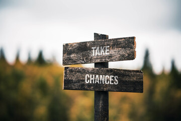 vintage and rustic wooden signpost with the weathered text quote take chances, outdoors in nature. blurred out forest fall colors in the background.