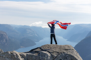 Woman with a waving flag of Norway on the background of nature - obrazy, fototapety, plakaty