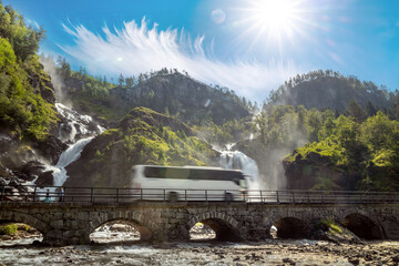 Tourist bus traveling on the road Latefossen Waterfall Odda Norway. Latefoss is a powerful, twin...