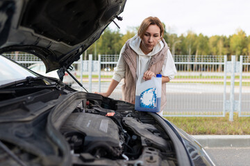 Fototapeta na wymiar mature woman pours coolant into the engine of a broken car