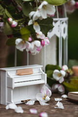Fototapeta na wymiar A beautiful postcard. A white piano, a statuette, candles, a book and a vase with a bouquet of blooming apple trees. A beautiful still life. The concept of classical music, poetry.