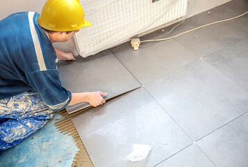 Tiler lays stoneware tiles on the floor