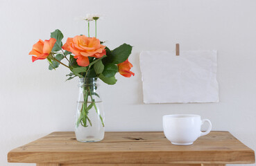 Orange roses bouquet. Old wooden bench, table. Blank vertical picture frame mockup. White wall...