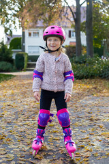 Smiling child girl in a helmet in protection rollerblades in the park