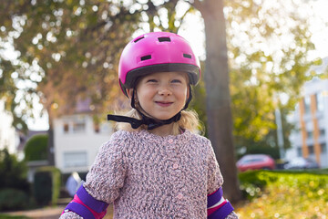 Smiling child girl in a helmet in protection rollerblades in the park