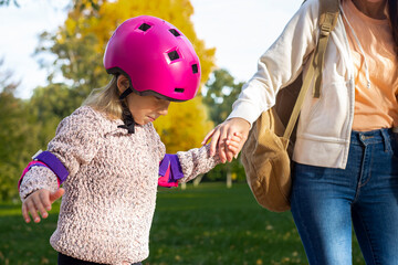 Mom teaches little daughter to roller skate in autumn park
