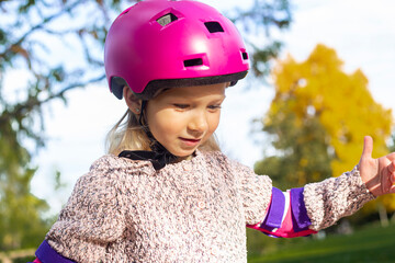 Smiling child girl in a helmet in protection rollerblades in the park