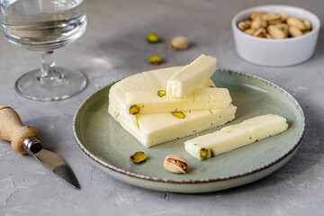 Italian cheese asiago with pistachios on stone black cutting board with cheese knife, pistachios in bowl and green napkin