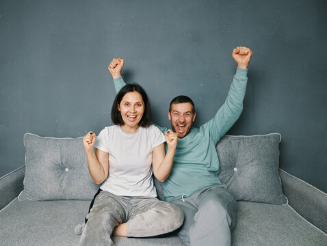 Excited happy male and female with winning gesture celebrate good news sitting on sofa at home