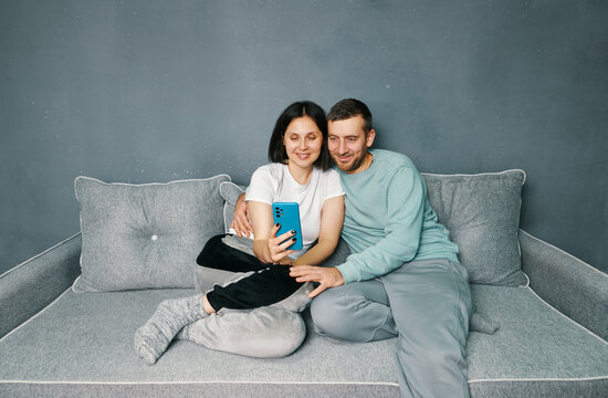 Young couple relaxing on sofa using mobile smart phone relaxing at home