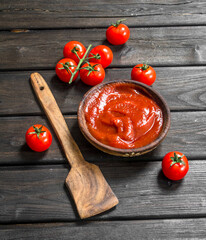 Tomato sauce in bowl with wooden scoop and cherry.