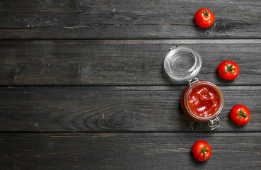 Tomato sauce in a glass jar and fresh tomatoes.