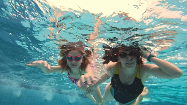 Young mother girl with preteen daughter child swimming in pool under water together wearing glasses googles. Family diving lessons