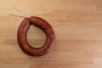 Top view of fermented circular traditional sausage on wooden background with text area.