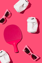 Table tennis racket, beverage cans and sunglasses on magenta background. Flat lay. Summer concept.
