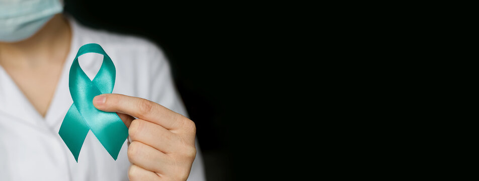 Doctor holds in his hand Teal ribbon on black background. Symbolic for cervical cancer, ovarian cancer, gynecological cancer and PCOS. And sexual assault awareness. Women's health care