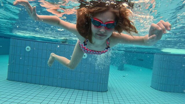 Beautiful preteen girl child swimming in pool under water wearing glasses googles. Pretty female kid diving in blue water at summer