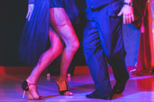 Dancing shoes of a couple, couples dancing traditional latin argentinian dance milonga in the ballroom, tango salsa bachata kizomba lesson, festival on wooden floor, red, purple and violet lights
