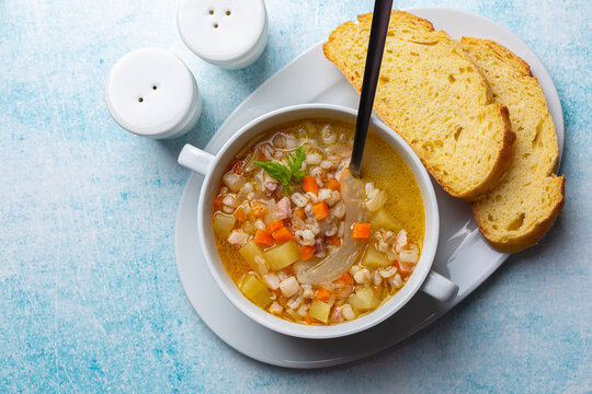 South Tyrolean barley soup Gerstsuppe, Graupensuppe, made with smoked pancetta or bacon, calery, fennel, potato, onion. Fresh bread.  Or Zuppa d'orzo. Light blue table surface.