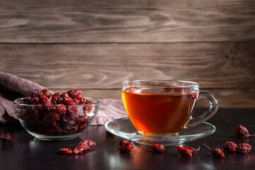 A cup of brewed berry tea and dried rose hips on a wooden table
