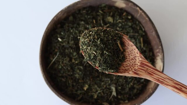 Dried nettle leaves for making medicinal tea in a wooden spoon on a beige background with a plate.