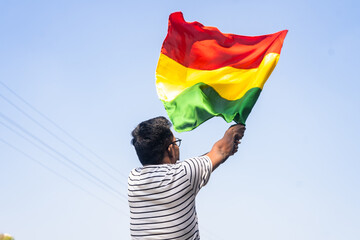 Back view shot of man waving black history month flag against sky - concept of freedom,...