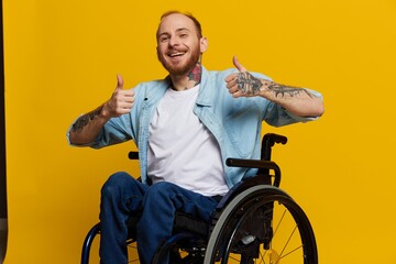 A man in a wheelchair smile and happiness, thumb up, with tattoos on his hands sits on a yellow...