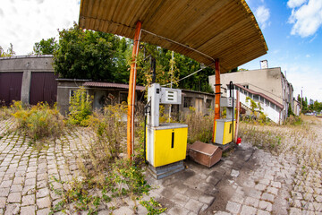 Old rusty gas station and dispensers abandoned and overgrown with vegetation on a sunny day. Summer.