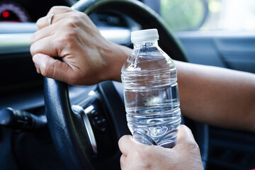 Asian woman driver hold cold water for drink in car, dangerous and risk an accident.