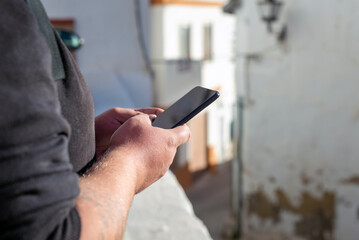 Man holding smartphone and searching information outdoor. Traveler in a black hoodie using smarphone in a city street