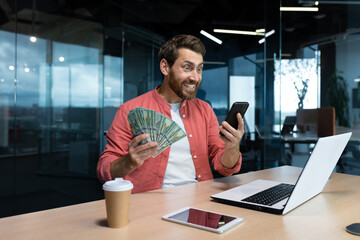 Successful businessman in red shirt celebrating victory and good achievement holding phone and...