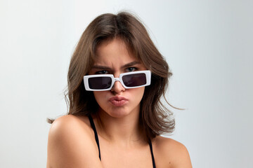 Naklejka premium Doubts. Portrait of young stylish beautiful girl in fashionable eyewear isolated over grey background. Concept of beauty, skin care, cosmetology, fashion, makeup