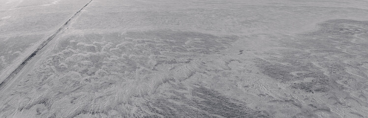 Aerial looking down onto a large snow covered farm field with a narrow road cutting across the left side of the frame.
