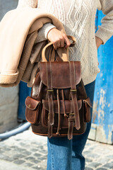 Part photo of a woman with a brown leather backpack with antique and retro look. Outdoors photo