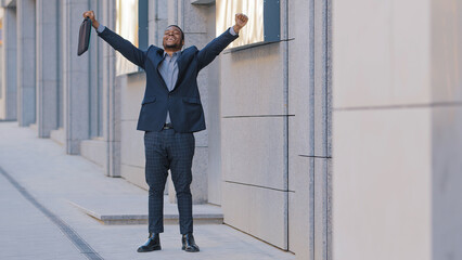 Overjoyed happy success African American man worker manager intern businessman winner walk outdoors...