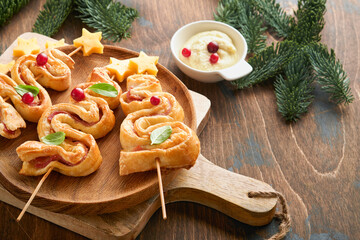 Christmas or New Year appetizer. Christmas tree shape puff pastry buns with cheese and ham. Group of Christmas tree shapes on wooden board. Festive idea for Christmas or New Year dinner. Top view.