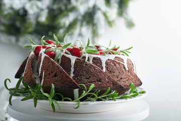 Christmas chocolate bundt cake. Traditional Christmas fruit cake with white glaze, cranberries and rosemary on white stand with Christmas decoration. Winter baking at Xmas or New Year. Copy space.