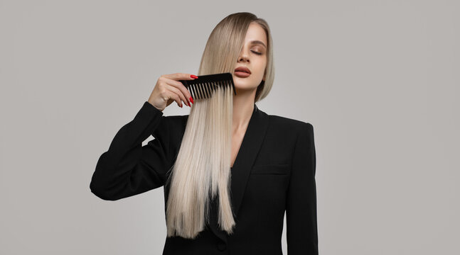Luxurious blonde combing her long hair. Grey background.
