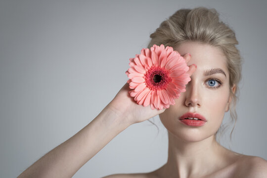 Beautiful young girl with clean skin and pink gerbera in her hand. Gray background.