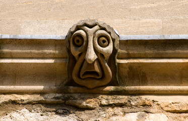 a comic stylized gargoyle with a fat face on a college wall in Oxford UK (New College)
